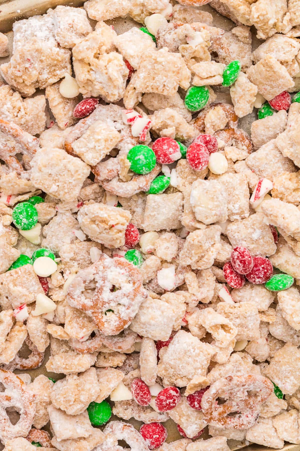 picture of muddy buddies chex mix with pretzels and red and green candies mixed in coated in powdered sugar