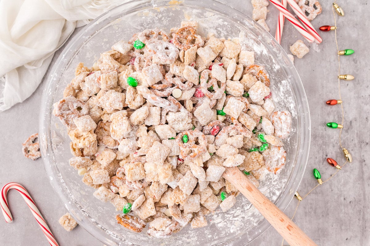 picture of muddy buddies chex mix with pretzels and red and green candies mixed in coated in powdered sugar