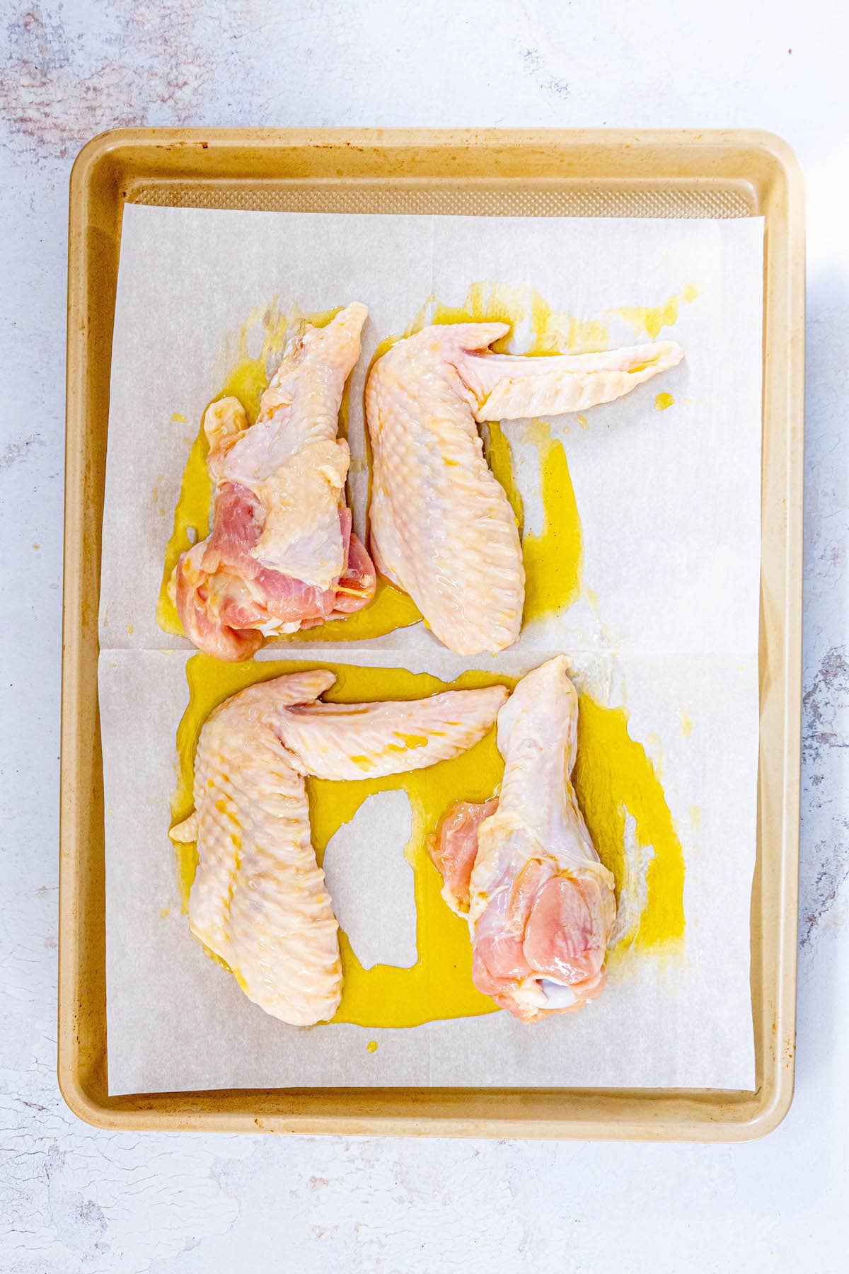 raw turkey wing pieces on a baking sheet lined with parchment paper drizzled in olive oil
