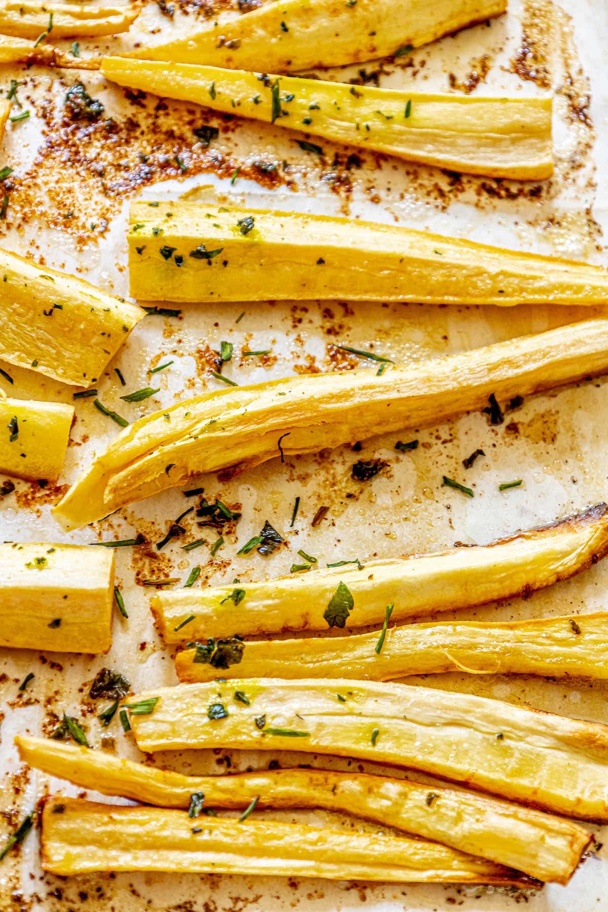 roasted parsnips on a baking sheet lined with parchment paper seasoned with garlic butter and herbs