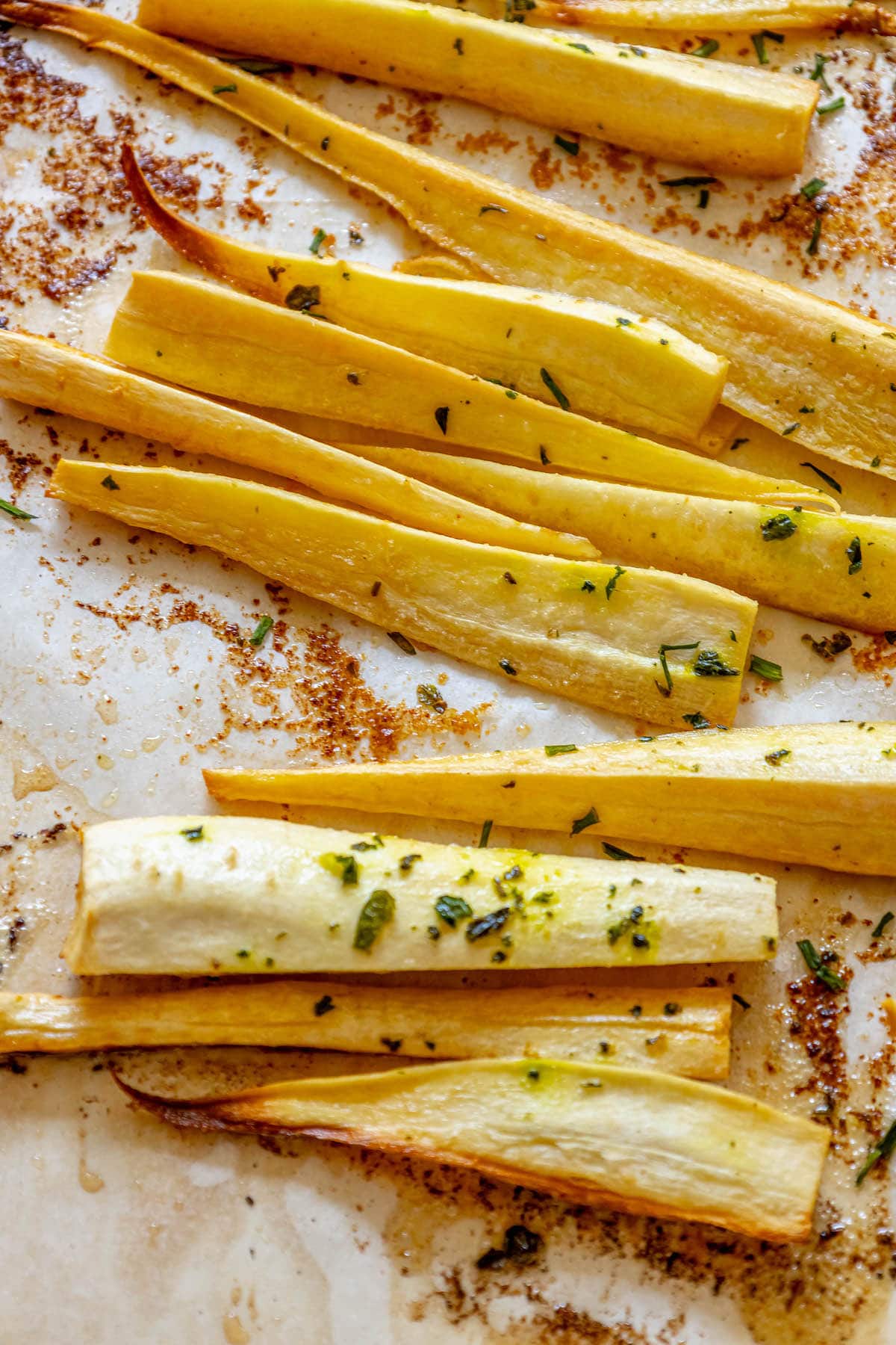 roasted parsnips seasoned with garlic butter and herbs on a baking sheet lined with parchment paper