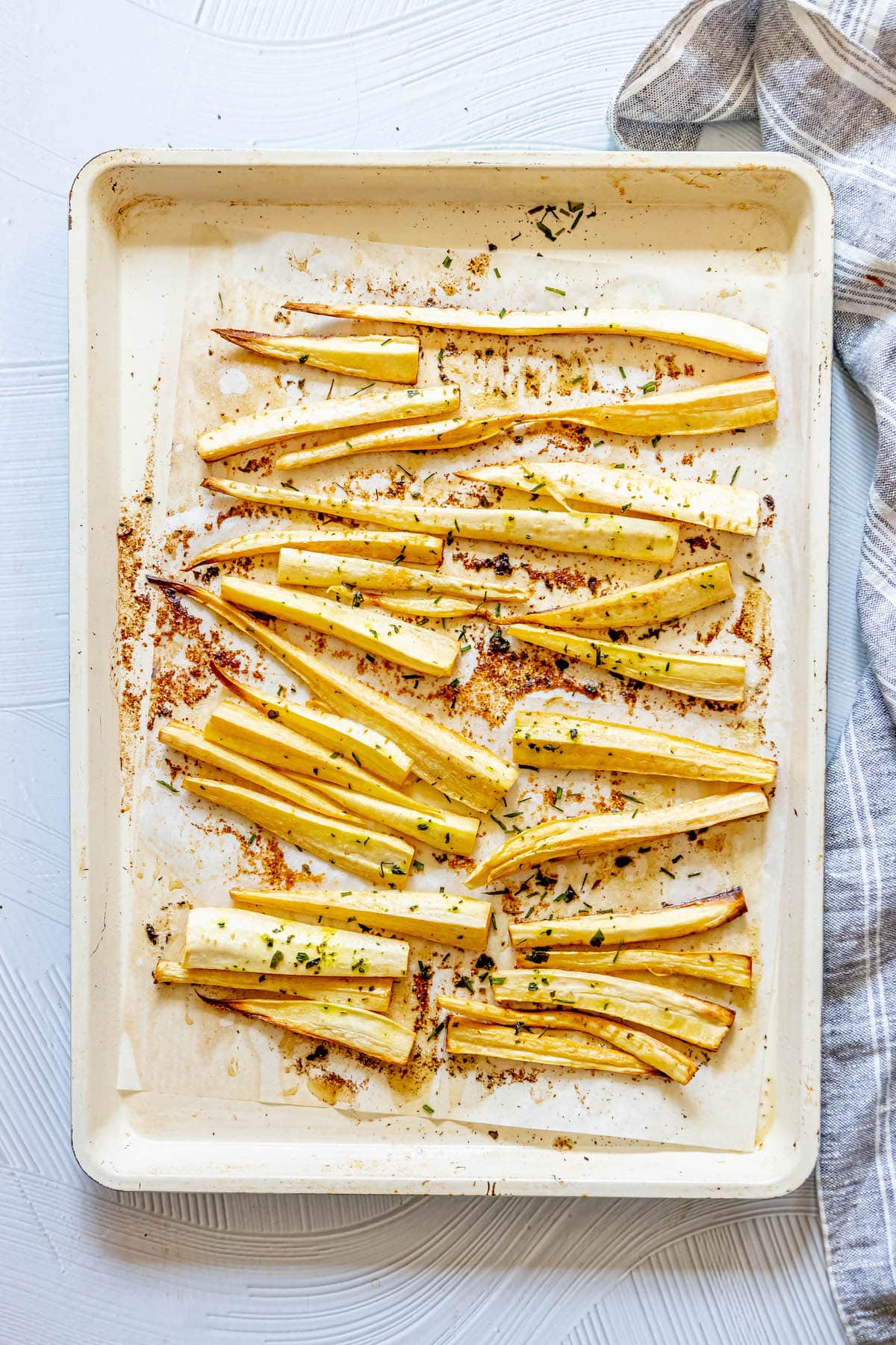 roasted parsnips on a baking sheet lined with parchment paper seasoned with garlic butter and herbs