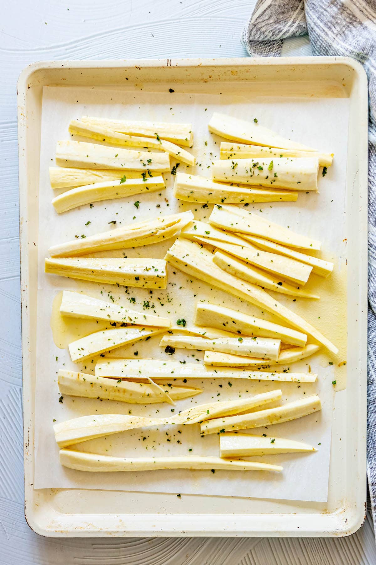 seasoned peeled and chopped parsnips on a baking sheet seasoned with herbs and garlic