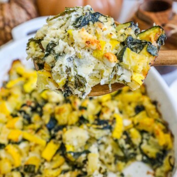 picture of spinach and zucchini feta baked casserole in a white dish with a spoon scooping it