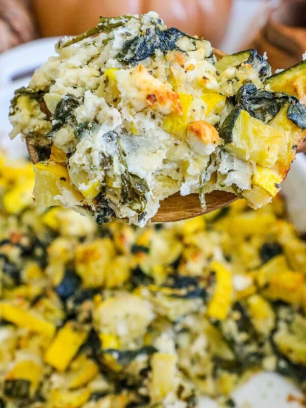 picture of spinach and zucchini feta baked casserole in a white dish with a spoon scooping it