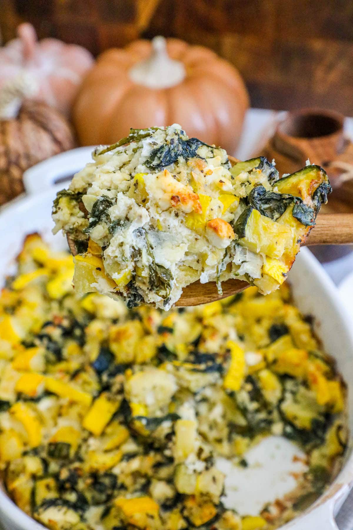 picture of spinach and zucchini feta baked casserole in a white dish with a spoon scooping it