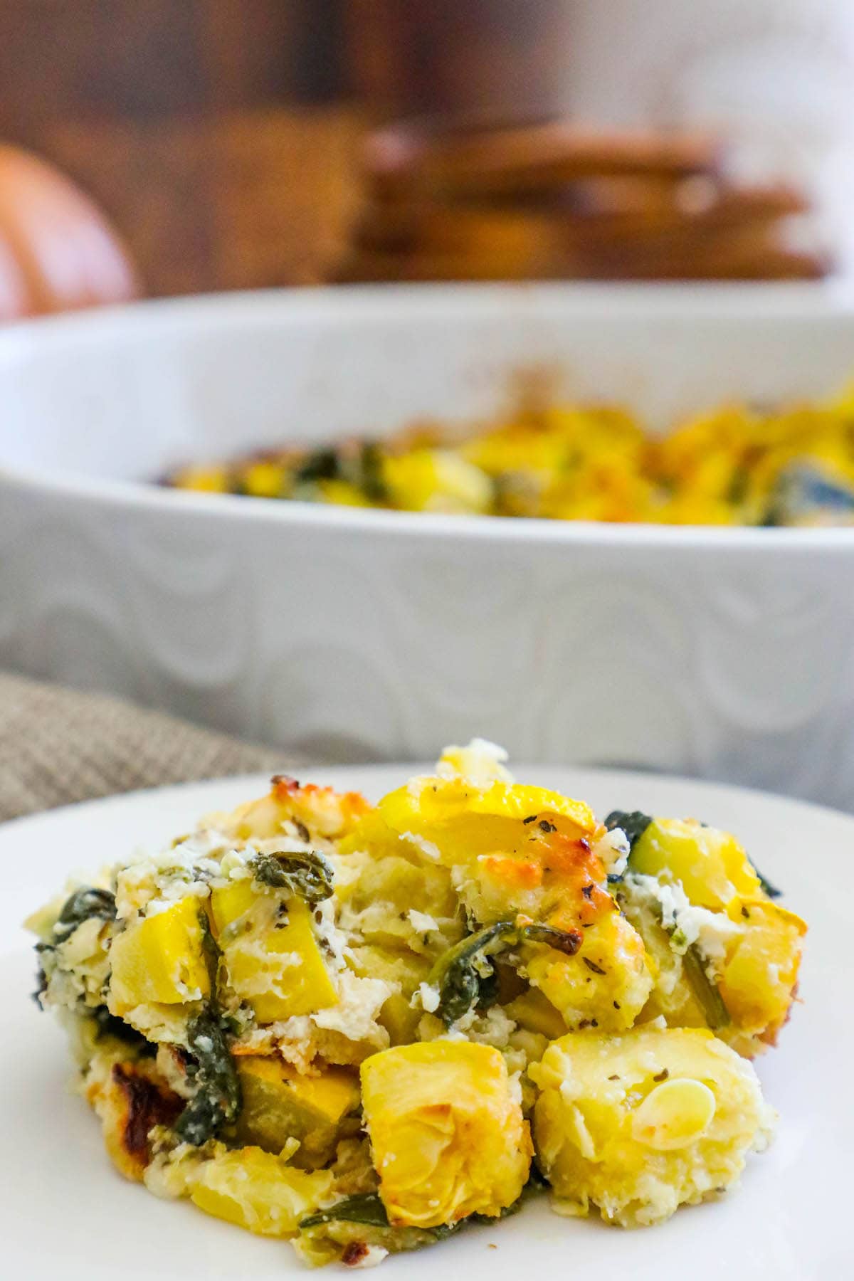 picture of a scoop of yellow and zucchini squash casserole on a white plate