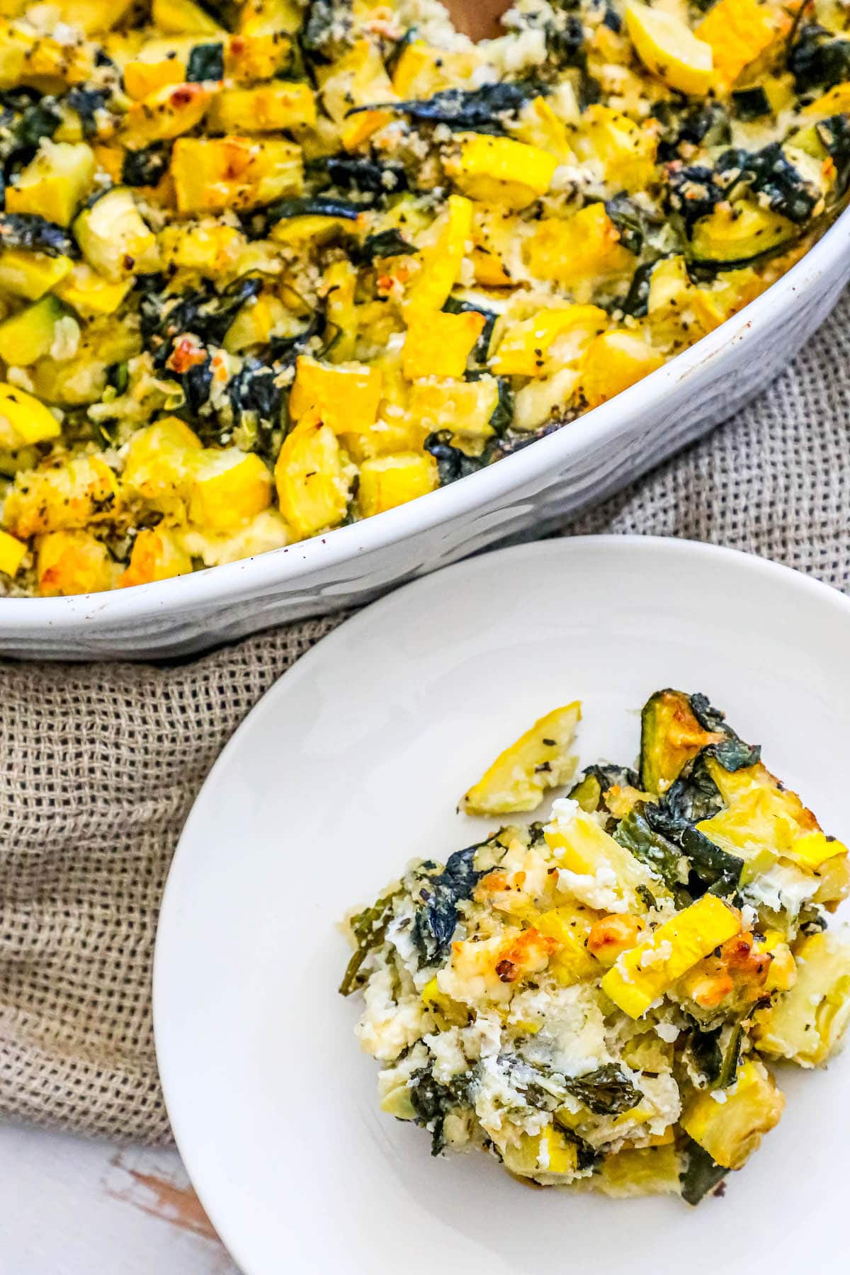 picture of spinach and zucchini feta baked casserole in a white dish with a plate of squash and zucchini scooped onto it