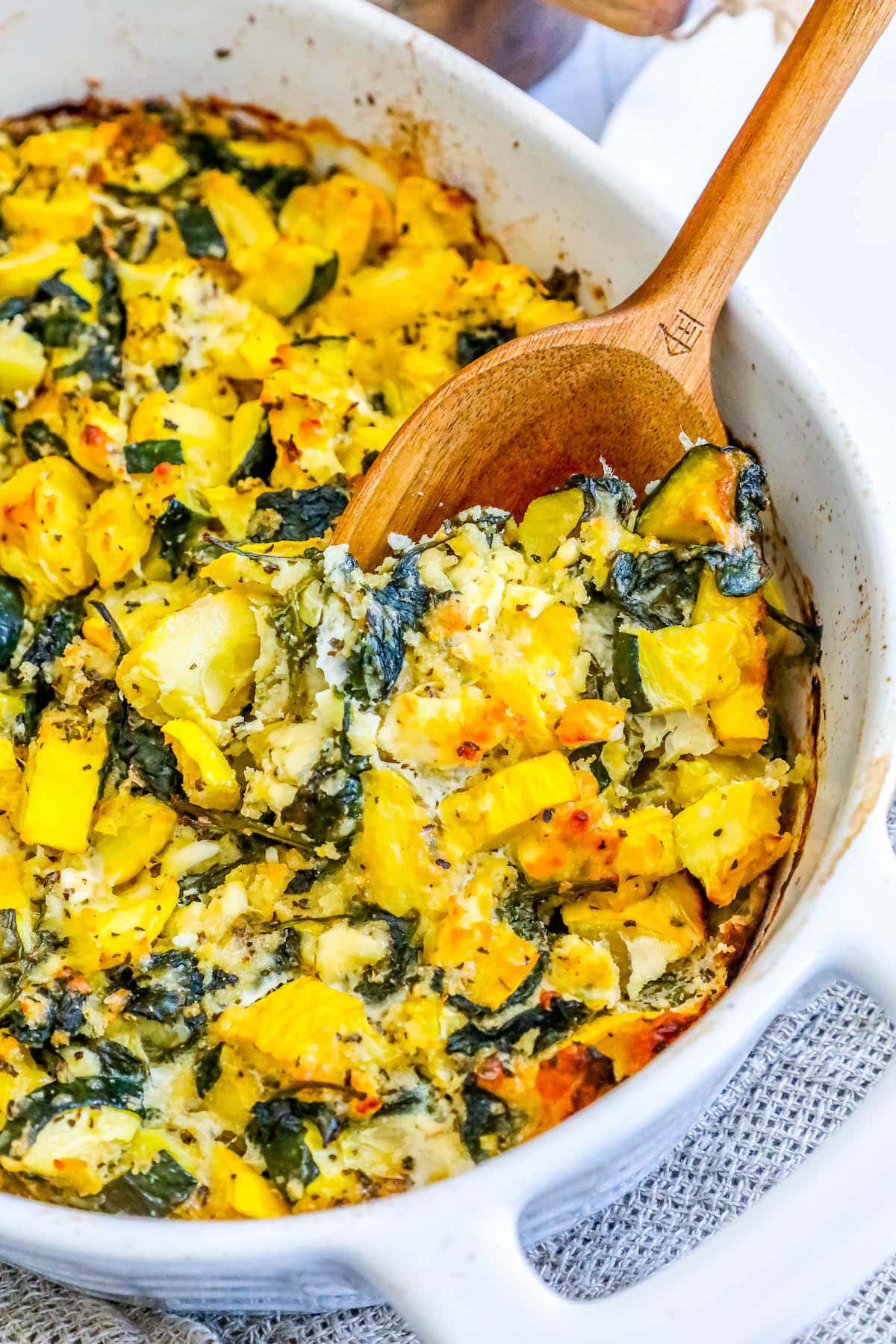 picture of spinach and zucchini feta baked casserole in a white dish with a spoon scooping it