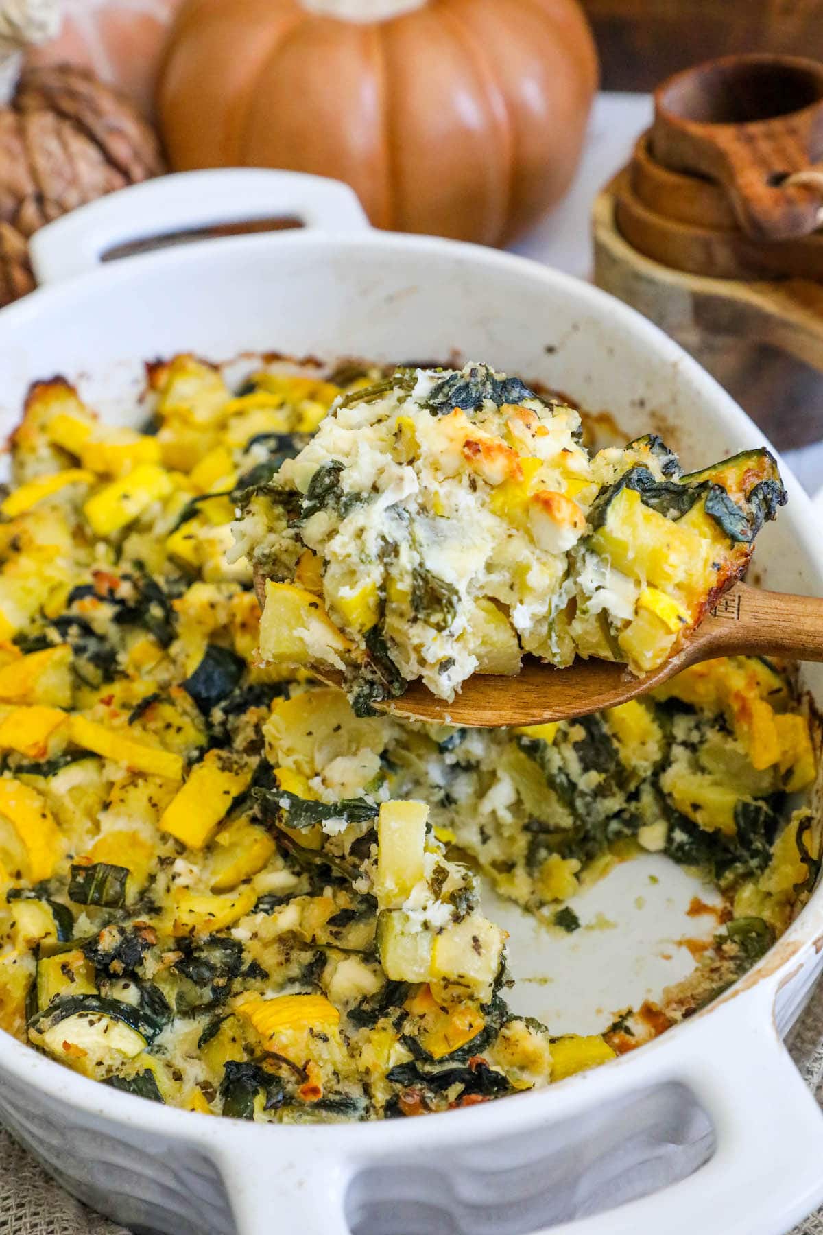 picture of spinach and zucchini feta baked casserole in a white dish with a spoon scooping it