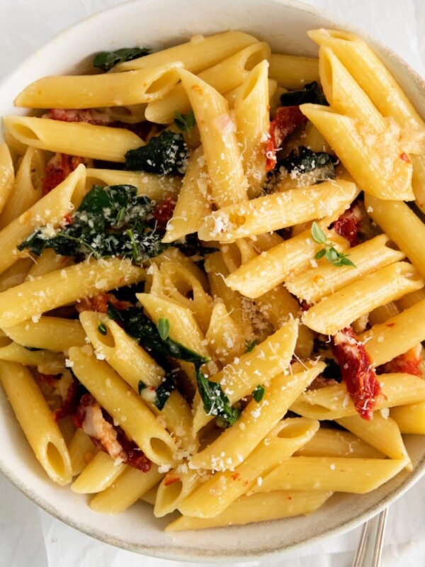 picture of penne pasta in a bowl with kale, sundried tomatoes, and cheese on a table with forks