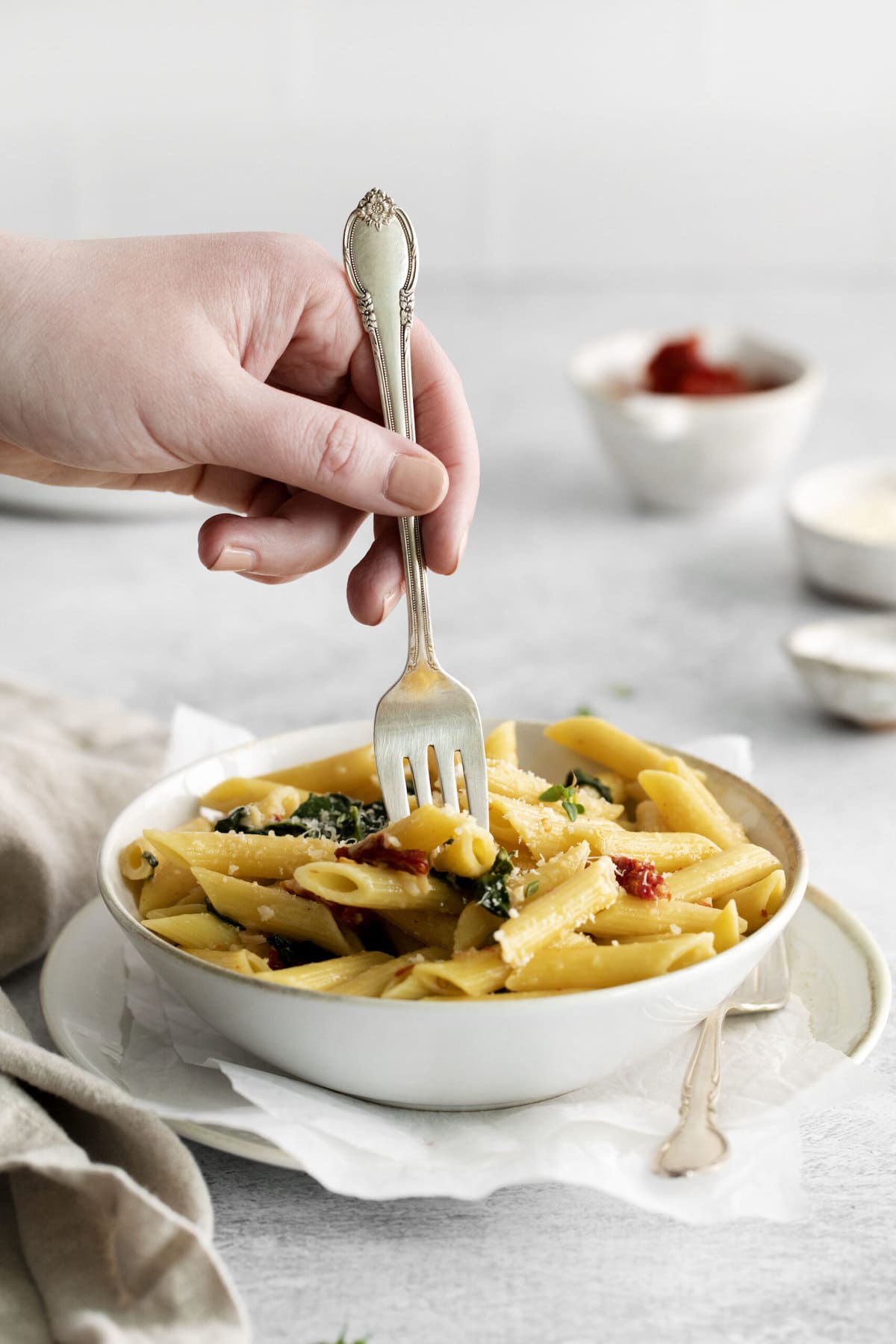 picture of penne pasta in a bowl with kale, sundried tomatoes, and cheese on a table with forks