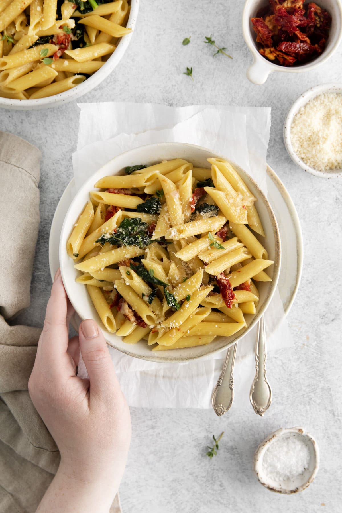 picture of penne pasta in a bowl with kale, sundried tomatoes, and cheese on a table with forks