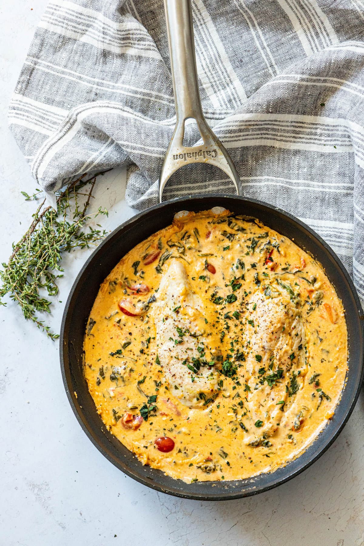 feta and spinach chicken bake in skillet, rosemary on the side, blue towel in background