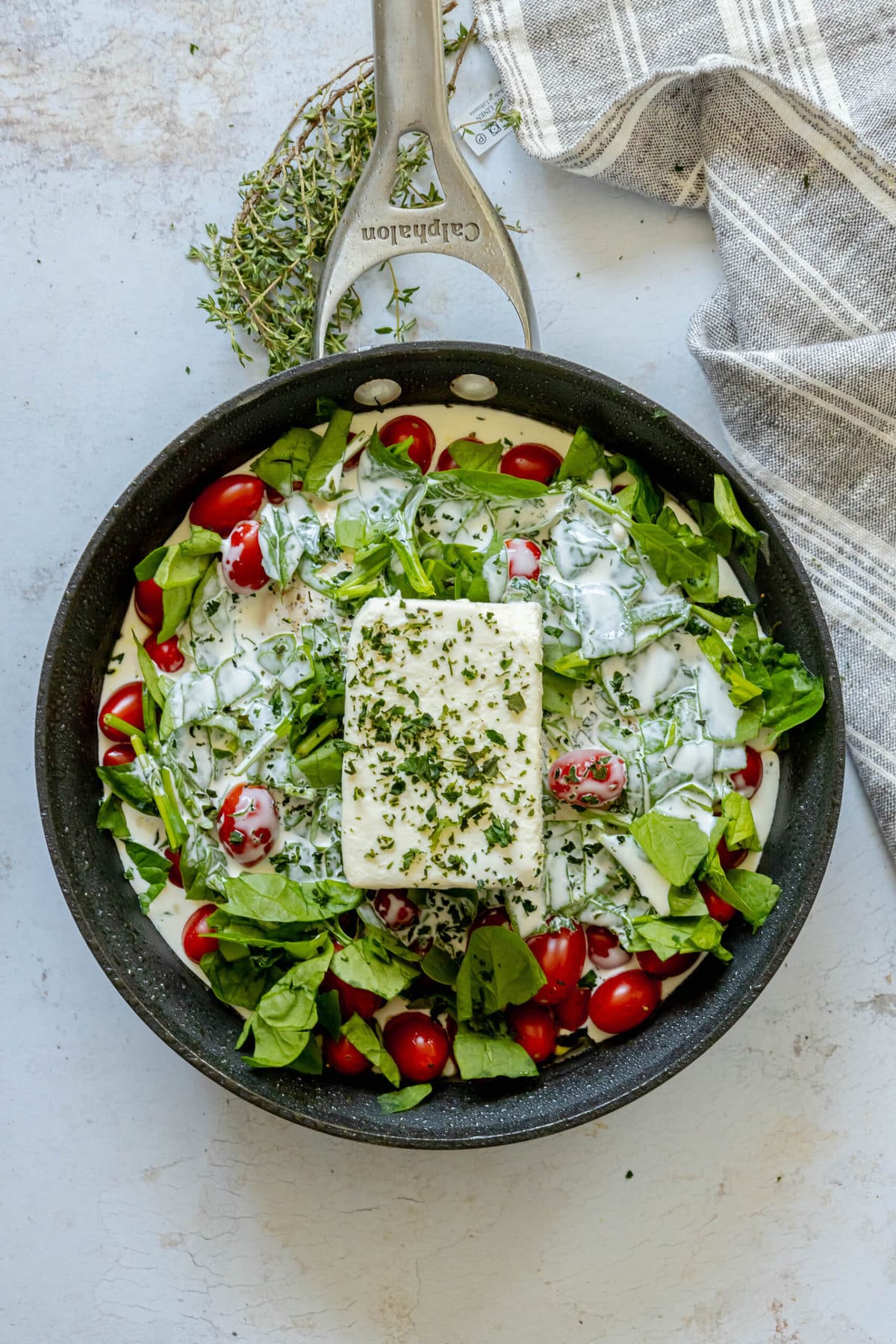 uncooked feta and spinach chicken bake in skillet with feta block on top