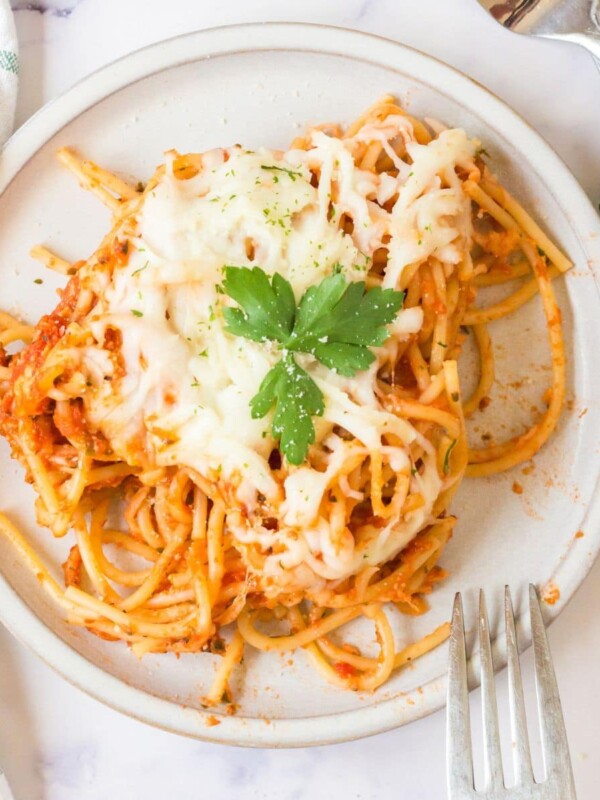 picture of baked spaghetti with melted cheese on a plate topped with basil with forks next to it