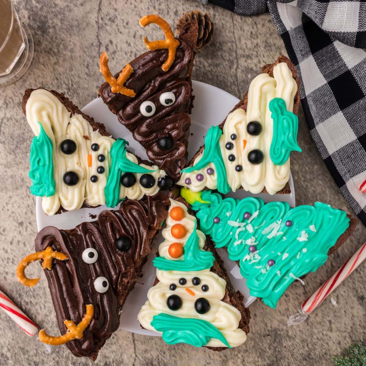 picture of brownies frosted to look like snowmen, christmas trees, and reindeer on a plate on a table