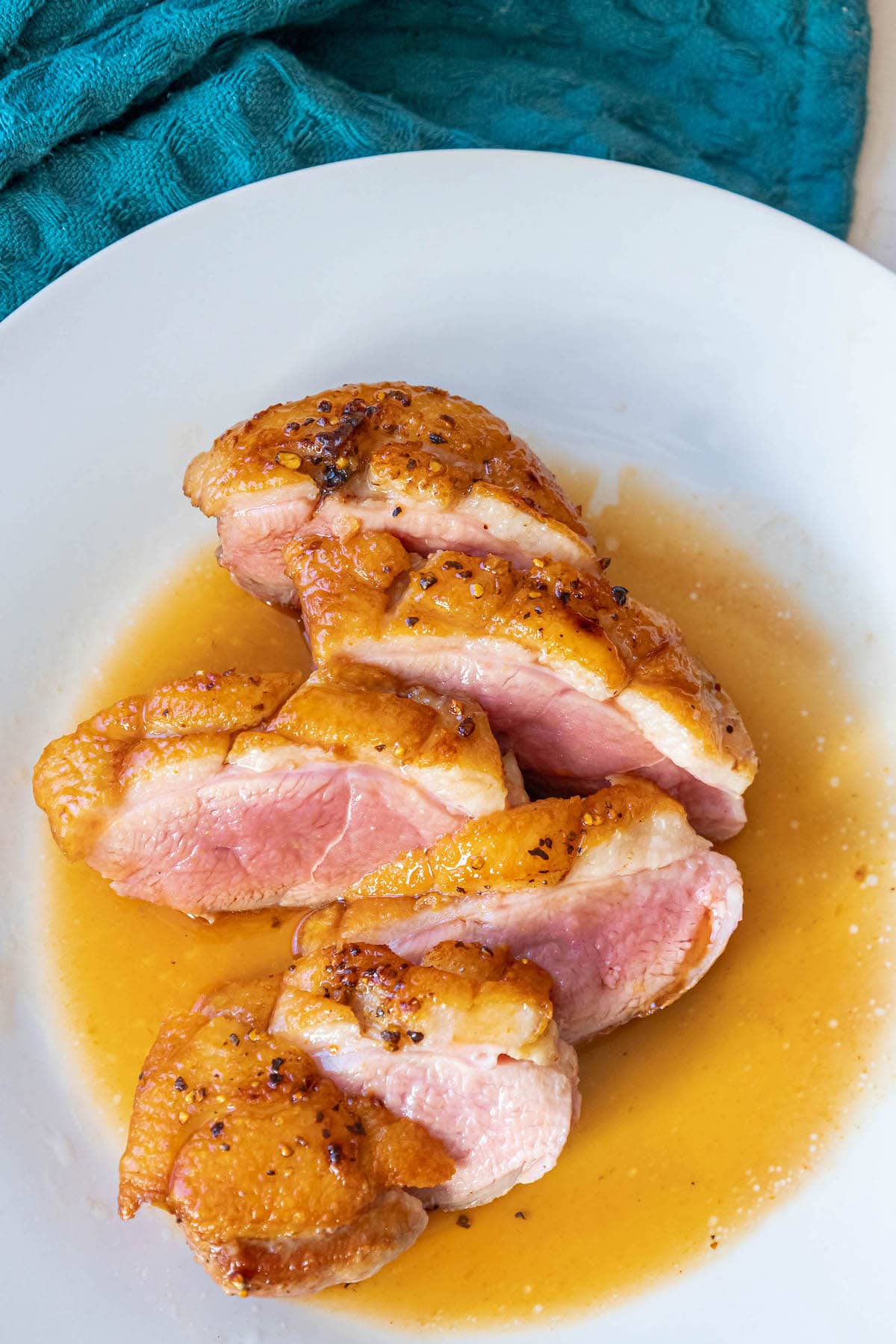 sliced duck breast with crispy fat  topped with an orange sauce on a plate