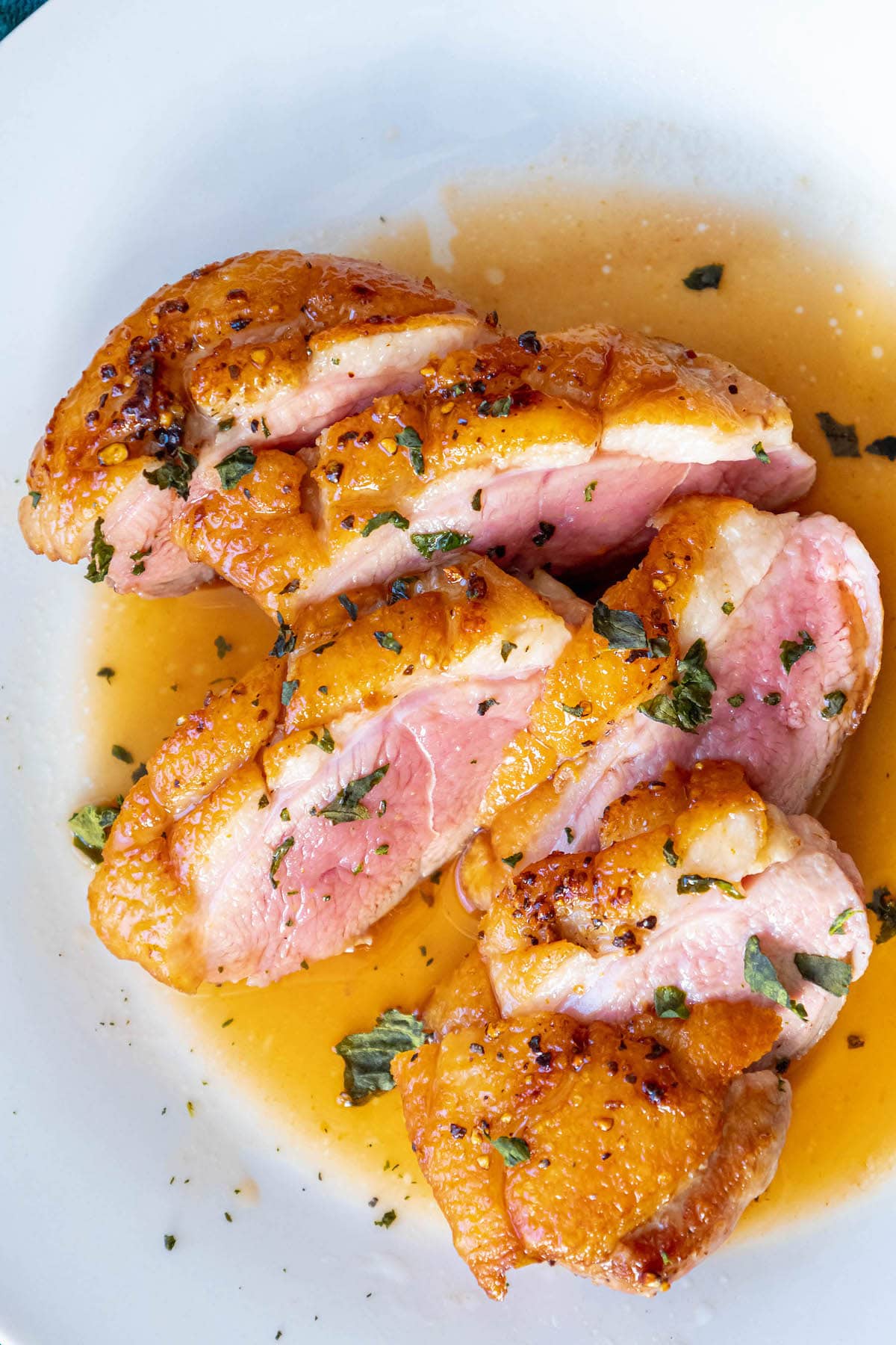sliced duck breast with crispy fat seasoned with salt, pepper, and herbs topped with an orange sauce on a plate