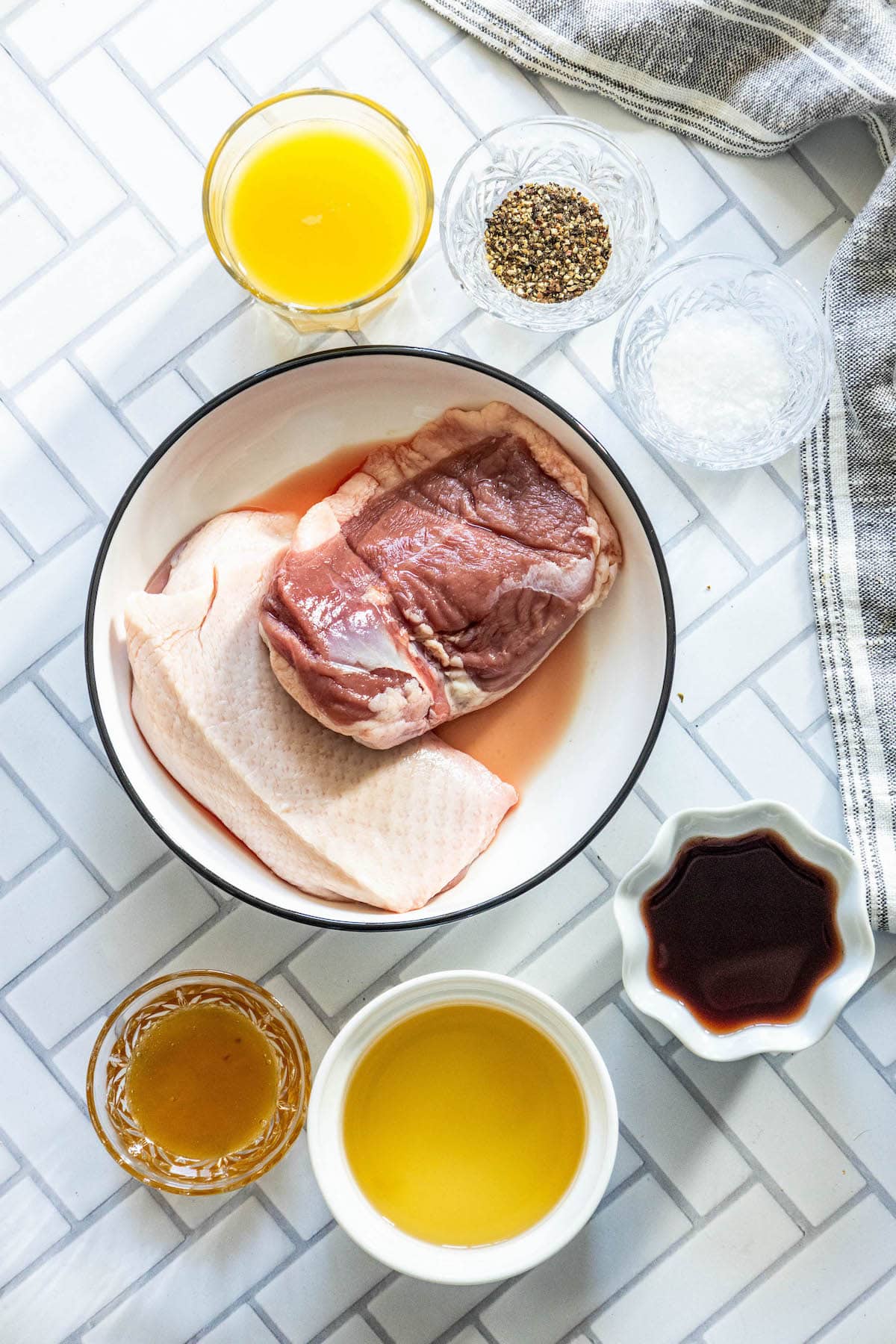 red wine, orange juice, honey, herbs, salt, pepper and raw duck breast on a table