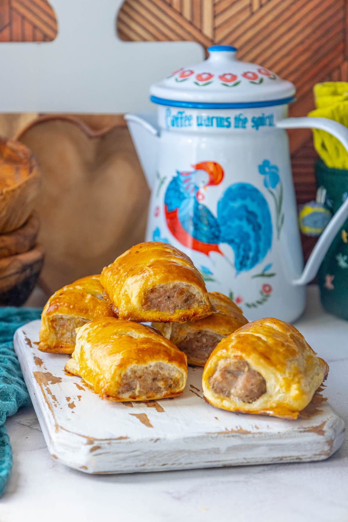 british sausage rolls on a white cutting board with a rooster tea pot in the background and wooden background
