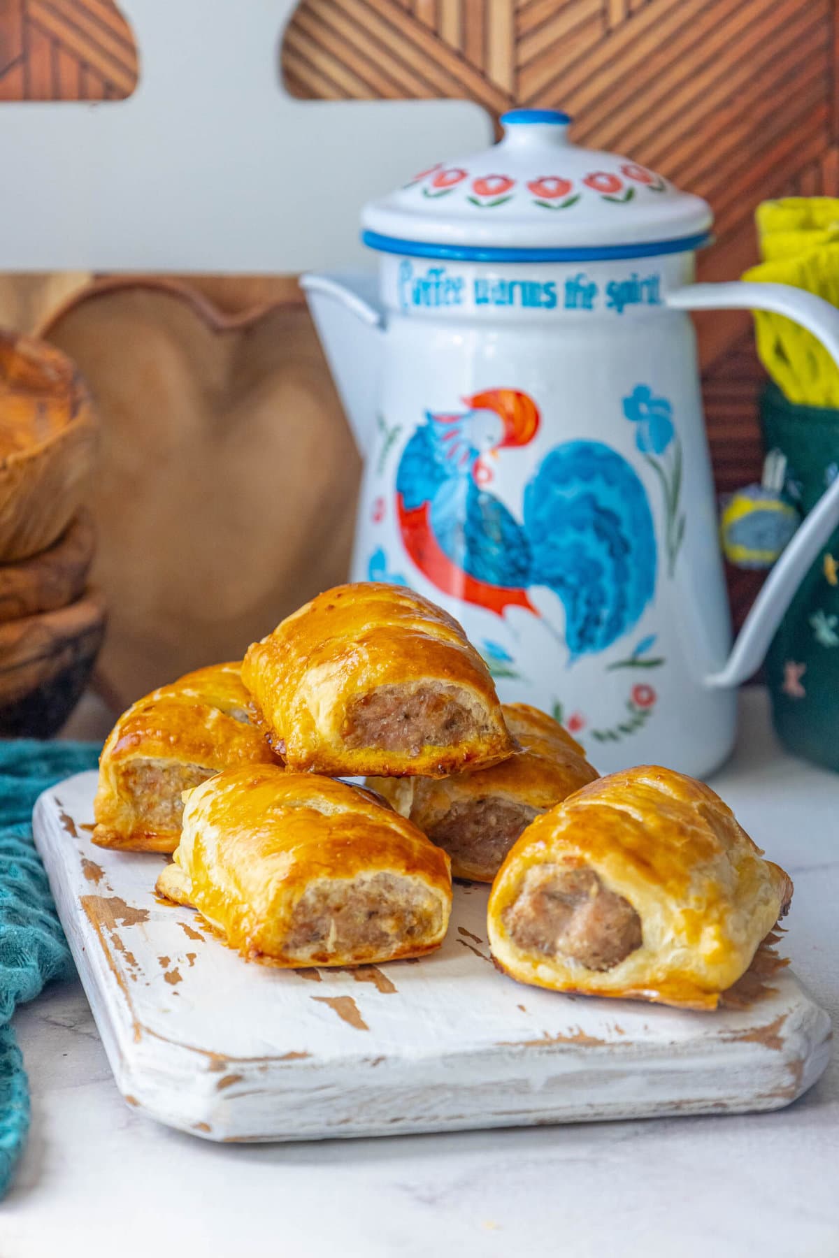 sausage rolls on a white cutting board rooster tea pot in background