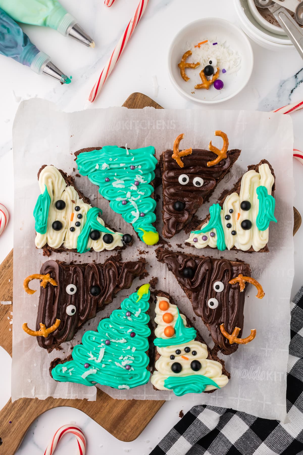 picture of brownies frosted to look like snowmen, christmas trees, and reindeer on a plate on a table