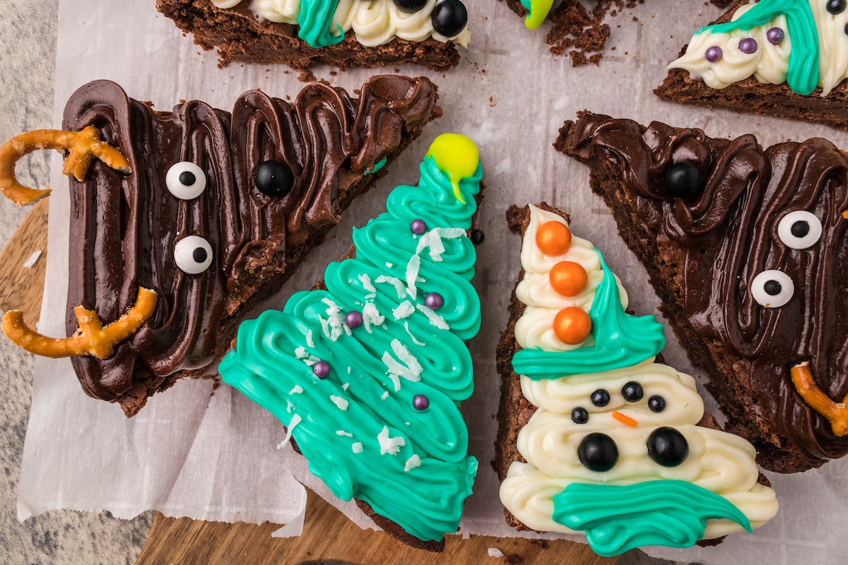 picture of brownies frosted to look like snowmen, christmas trees, and reindeer on a plate on a table