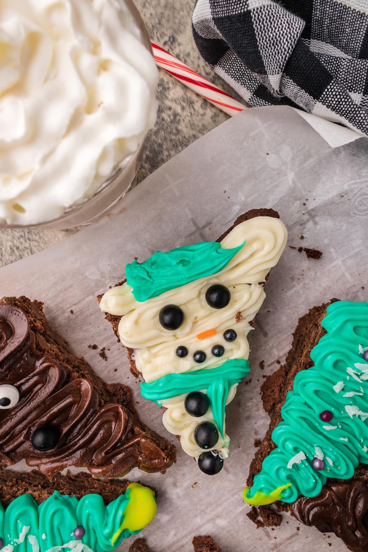 picture of brownies frosted to look like snowmen, christmas trees, and reindeer on a plate on a table