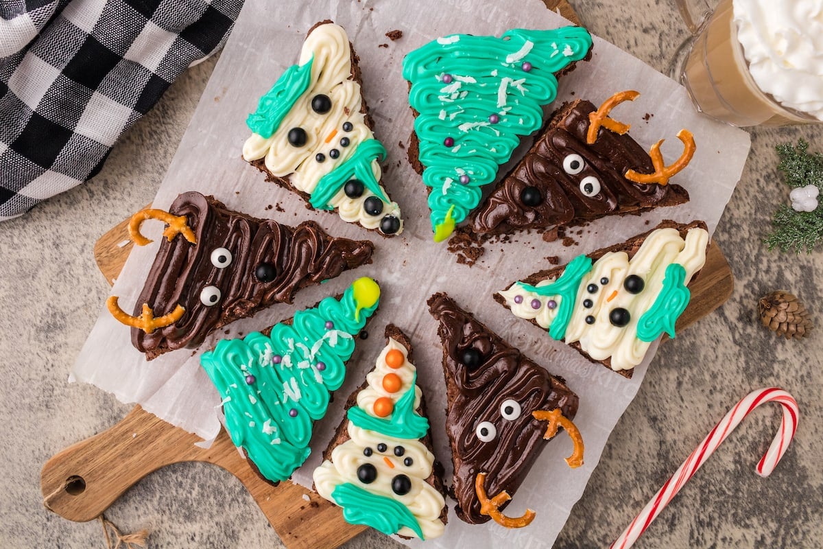 picture of brownies frosted to look like snowmen, christmas trees, and reindeer on a plate on a table