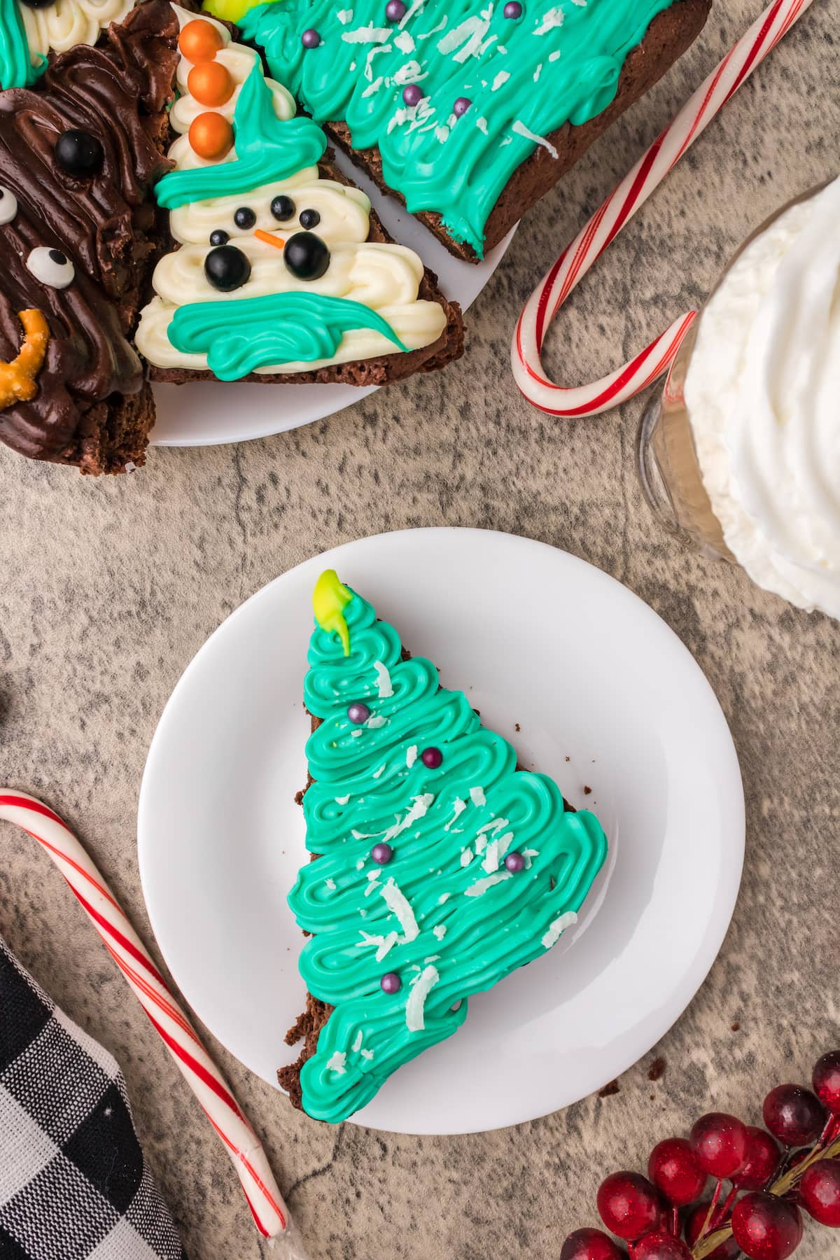 picture of brownies frosted to look like snowmen, christmas trees, and reindeer on a plate on a table