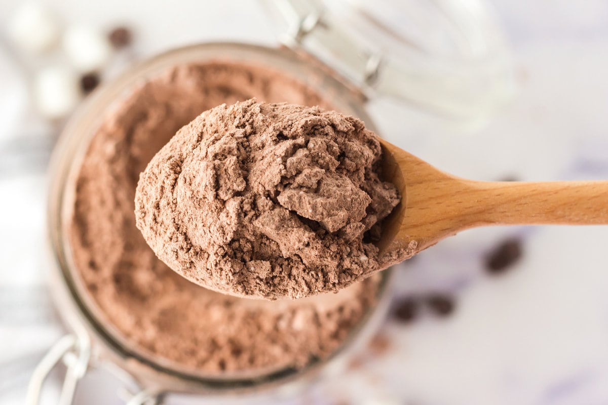 picture of homemade powdered hot cocoa mix on a spoon over cocoa mix in a jar