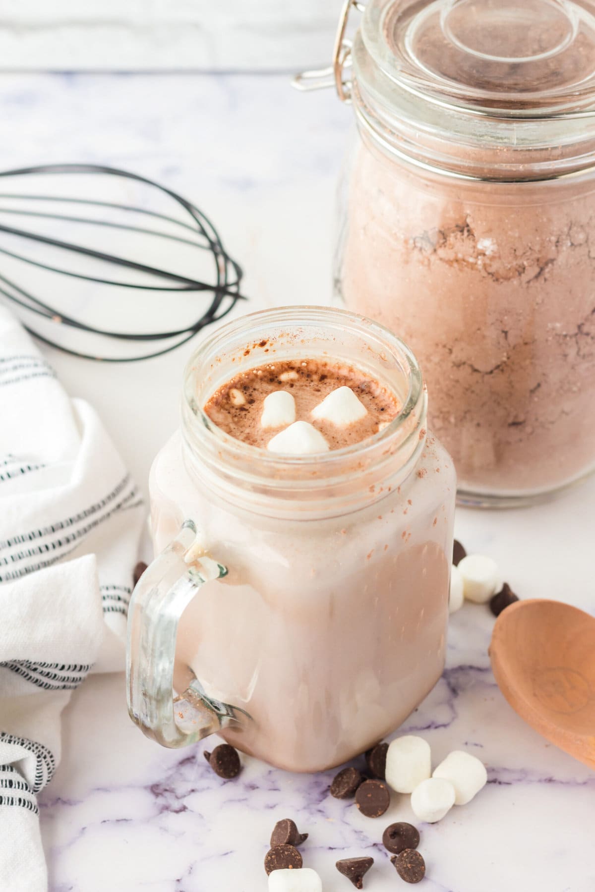 picture of hot cocoa in a mug with marshmallows on a table with marshmallows and chocolate chips scattered around