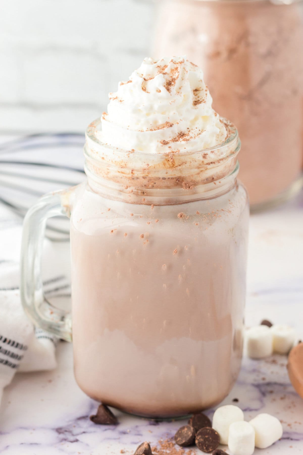 picture of hot cocoa in a mug with marshmallows on a table with marshmallows and chocolate chips scattered around