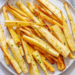 roasted parsnips seasoned with garlic butter and herbs on a white speckled plate