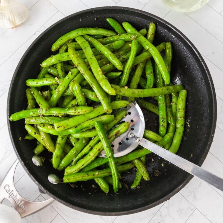 picture of green beans sauteed with garlic and herbs in a pan with a spoon on a table