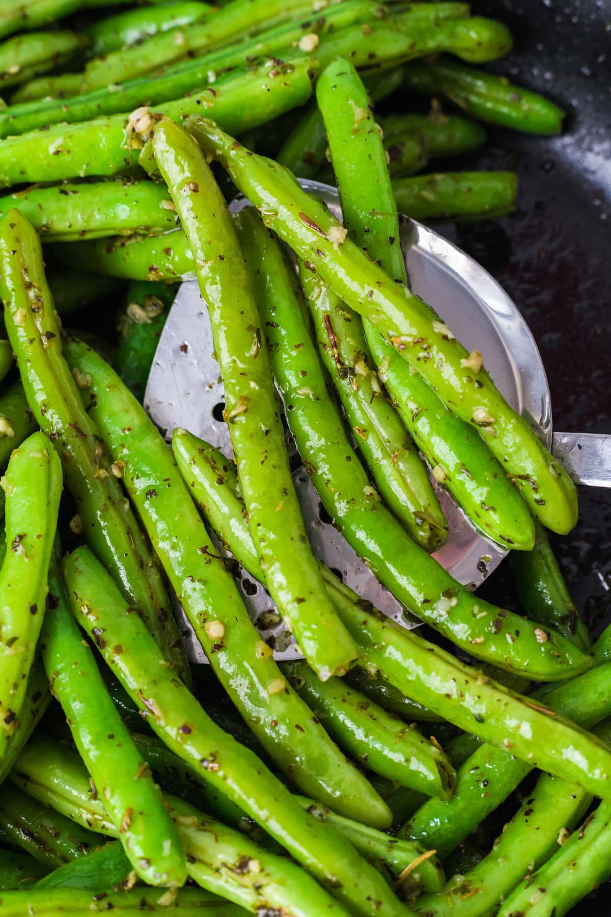 picture of green beans sauteed with garlic and herbs in a pan with a spoon on a table