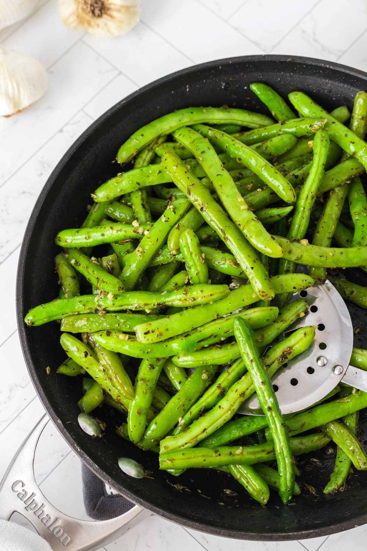 picture of green beans sauteed with garlic and herbs in a pan with a spoon on a table