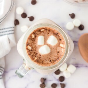 picture of hot cocoa in a mug with marshmallows on a table with marshmallows and chocolate chips scattered around