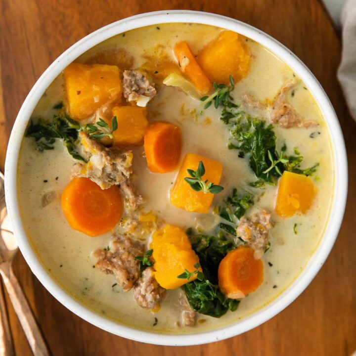 picture of creamy turkey and butternut squash chili with carrots, thyme,, kale and peppers in a white bowl on a table