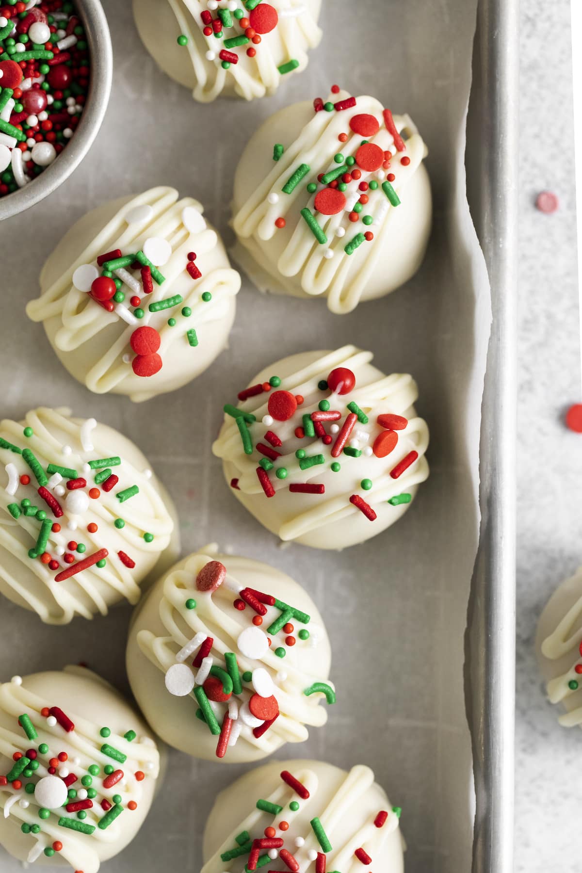 peanut butter truffles dipped in white chocolate and topped with christmas sprinkles on a baking sheet lined with parchment paper