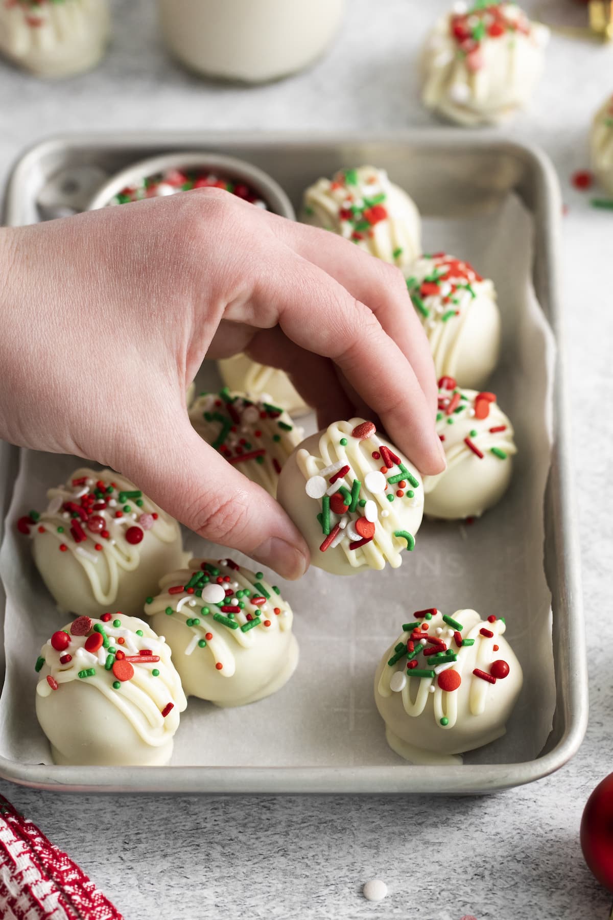 a hand holding peanut butter truffles dipped in white chocolate and topped with christmas sprinkles on a baking sheet lined with parchment paper