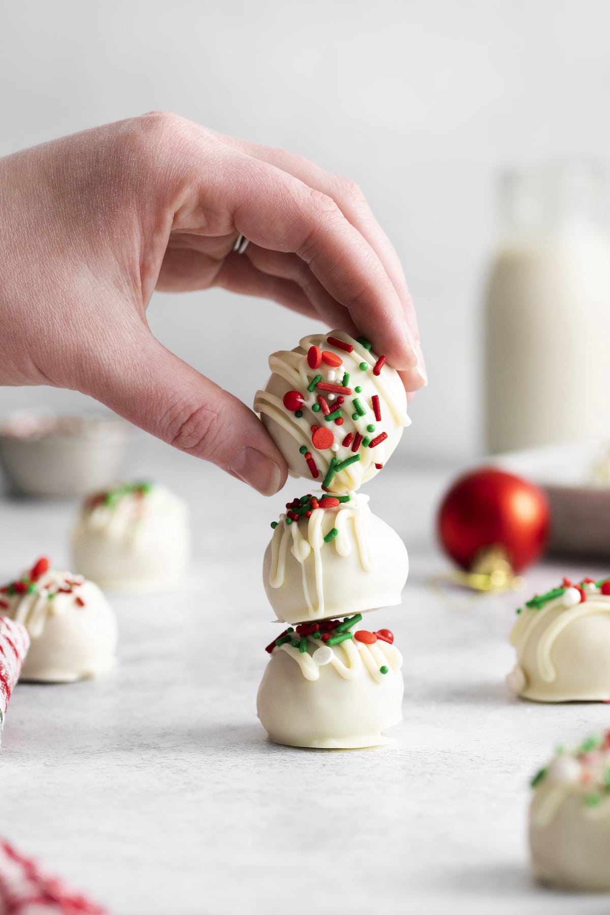 a hand stacking white chocolate dipped peanut butter truffles with christmas sprinkles on them 