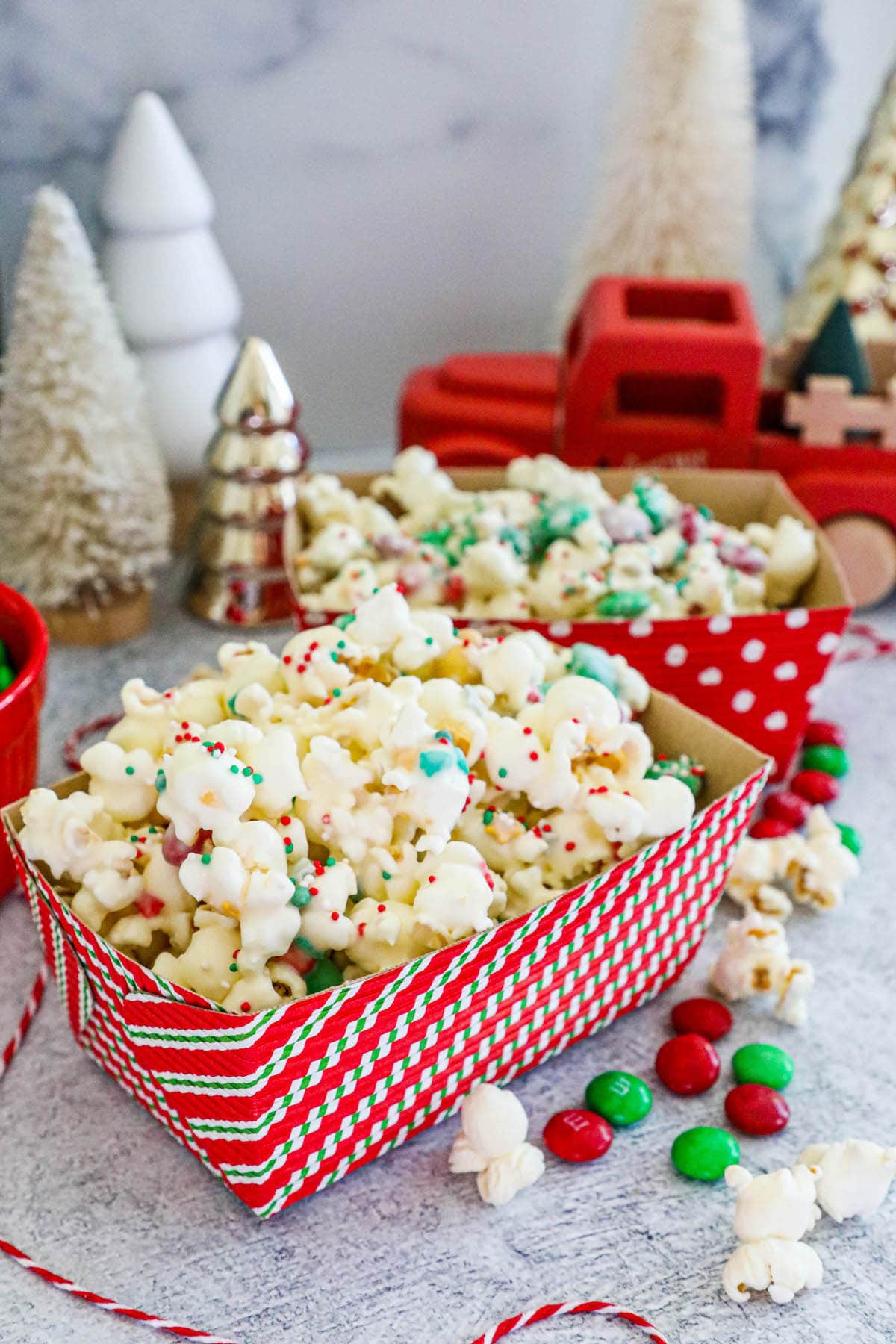 popcorn with candies in it in a striped box with Christmas trees in the background. 