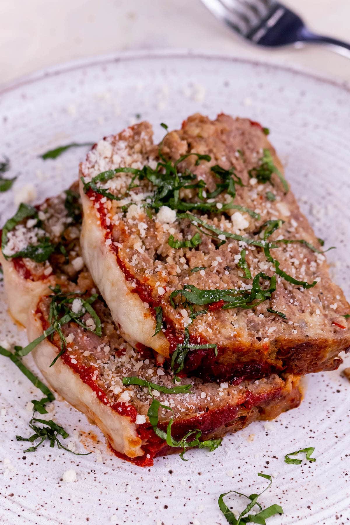 slices of meatloaf baked with melted mozzarella cheese and tomato sauce on a plate with ribbons of basil on top 