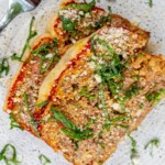 meatloaf slices baked in marinara sauce and mozzarella cheese with shredded basil and parmesan on a white plate