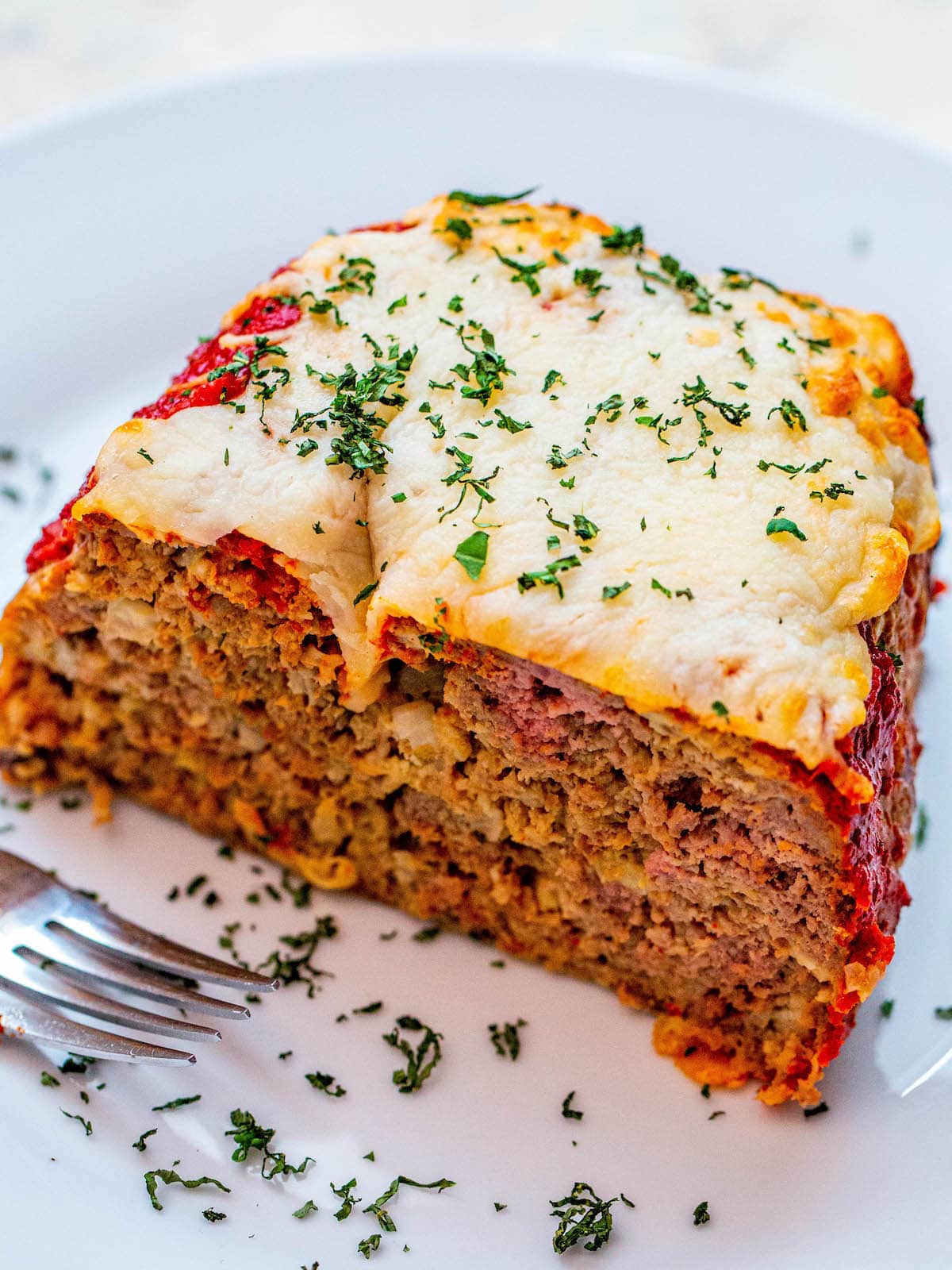 meatloaf covered in cheese and parsley on a white plate with a fork