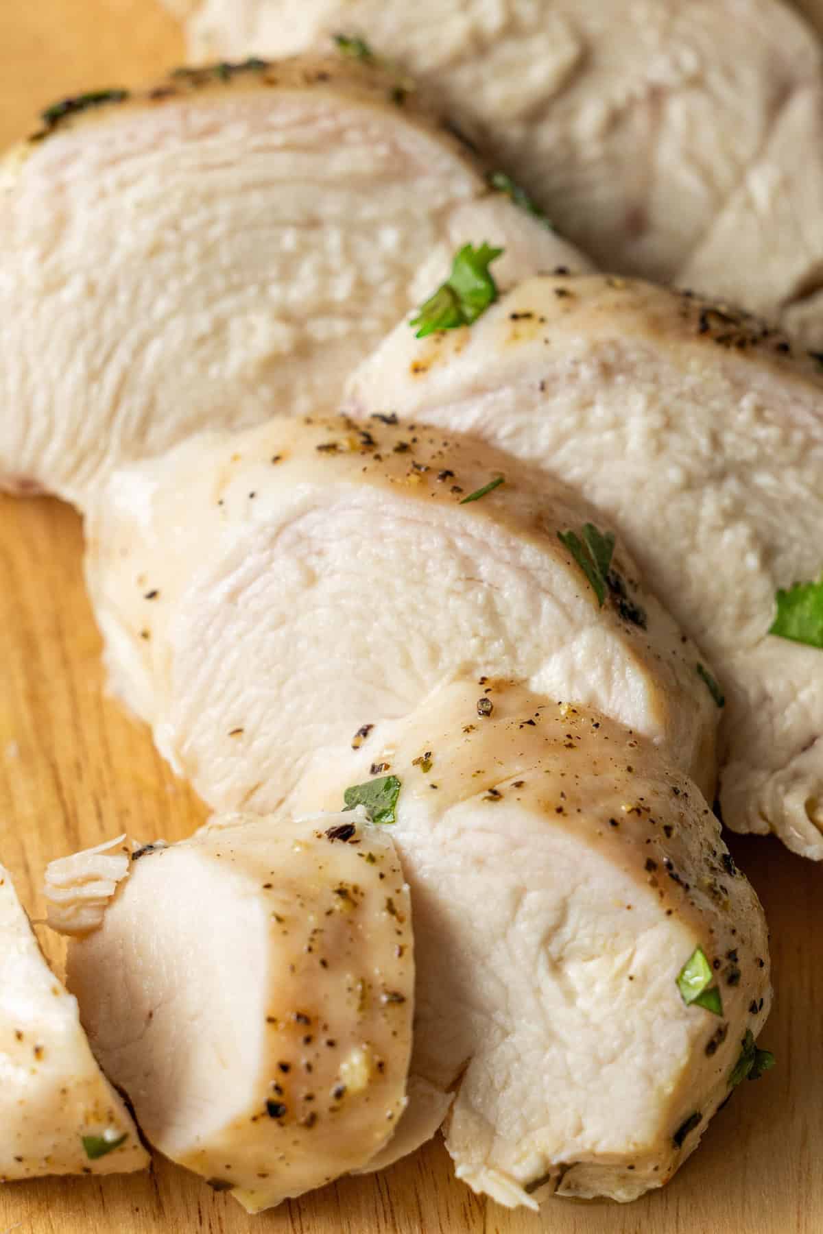 Close-up of sliced, cooked chicken breast seasoned with herbs and pepper, displayed on a wooden cutting board. This image showcases the best easy baked chicken breasts recipe, perfect for a quick and delicious meal.