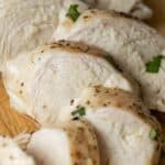 Sliced cooked chicken breast on a wooden cutting board, seasoned with herbs and black pepper. The Best Easy Baked Chicken Breasts Recipe ensures juicy and flavorful chicken every time.