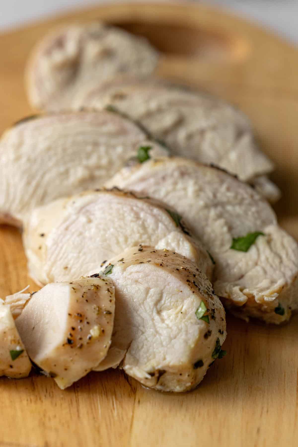 Sliced cooked chicken breast seasoned with herbs on a wooden cutting board, perfect for trying out the best easy baked chicken breasts recipe.